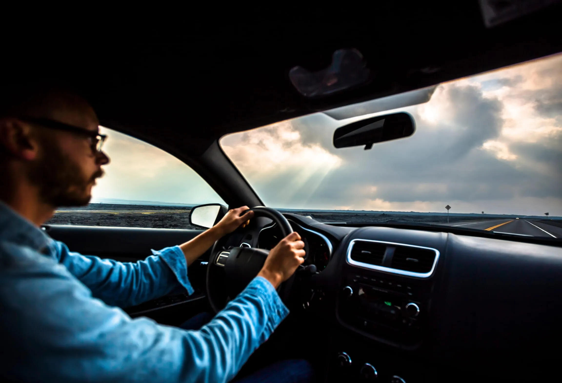 A man driving on the road with clouds in the sky